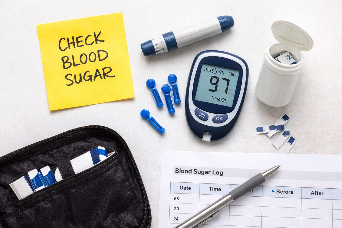 Kitchen counter with sugar testing tools including a smartphone, nutrition label, refractometer, and glucose test strips on a light marble surface